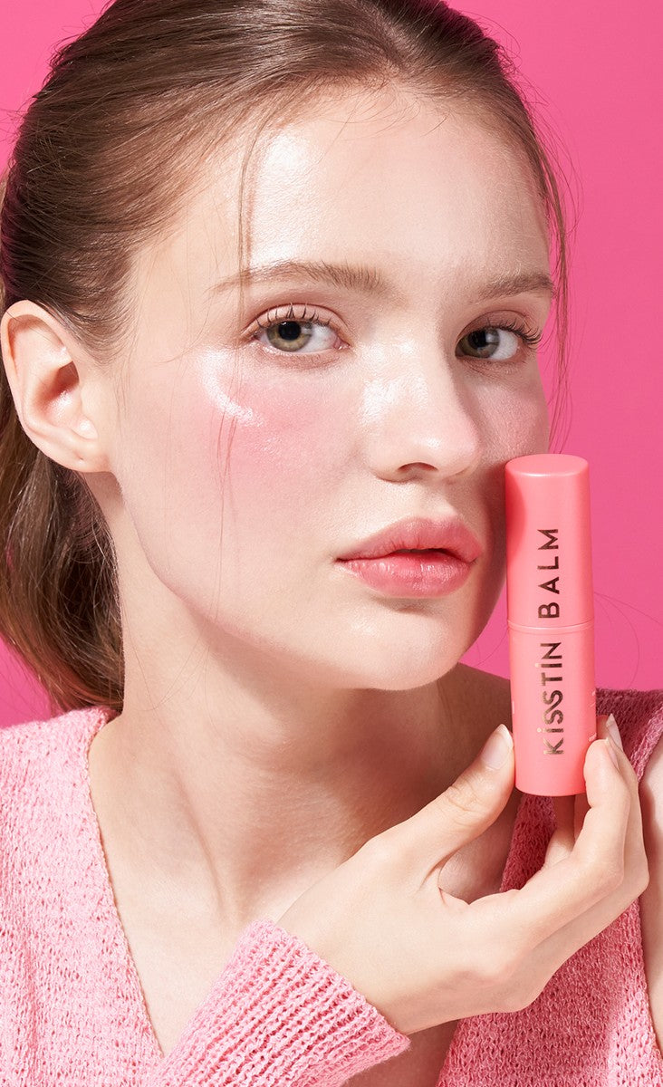 Woman with a sheer pink flush holding the KAHI Kisstin Balm stick