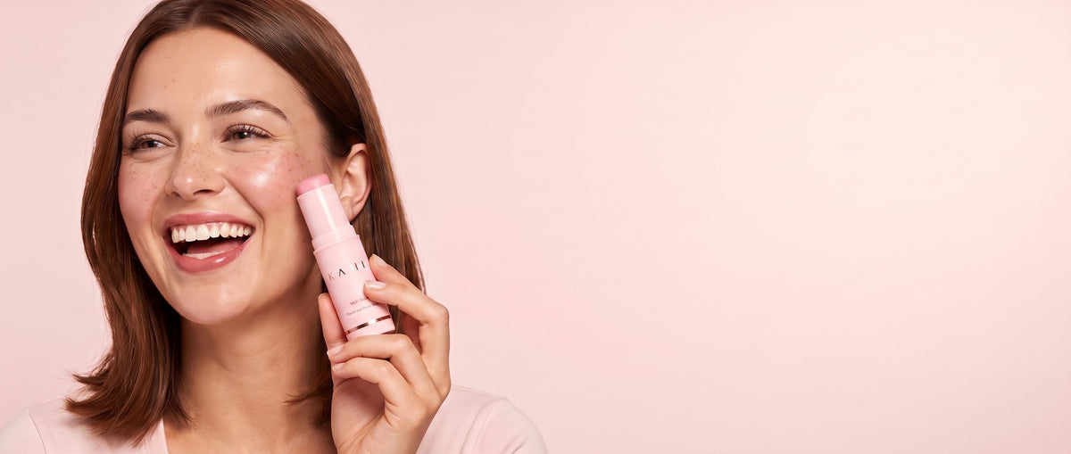 A young woman laughing as she holds the KAHI Multi Balm to her cheek